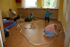 Spielende Kinder sitzen auf dem Fußboden und spielen mit einer Holzeisenbahn